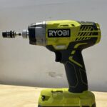 Close-up of a hand holding a Ryobi impact driver, showcasing its compact size and ergonomic design.