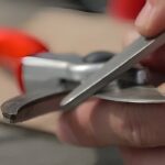 Close-up of hand cleaning pruning shears with steel wool and oil, demonstrating how to care for pruning tools and prevent rust.