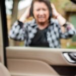 A woman looking through the window of her car with keys locked inside, expressing frustration.