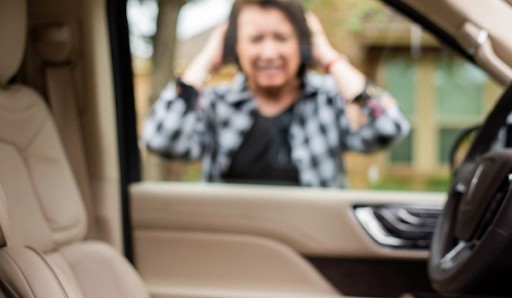 A woman looking through the window of her car with keys locked inside, expressing frustration.