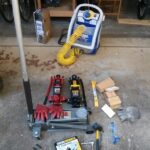 Tools used for DIY car battery removal, including jacks, wrenches, gloves, and safety glasses.