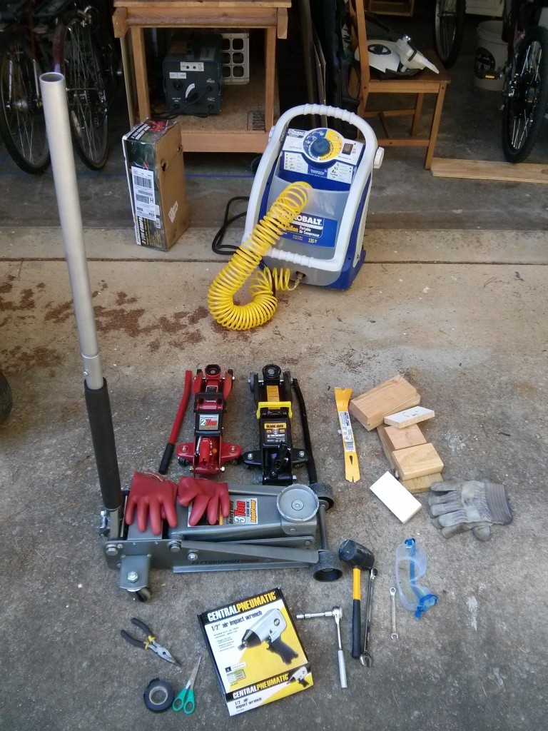 Tools used for DIY car battery removal, including jacks, wrenches, gloves, and safety glasses.