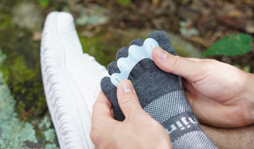 Person, wearing a variety of natural footgear, putting on a Correct Toes Original toe spacer